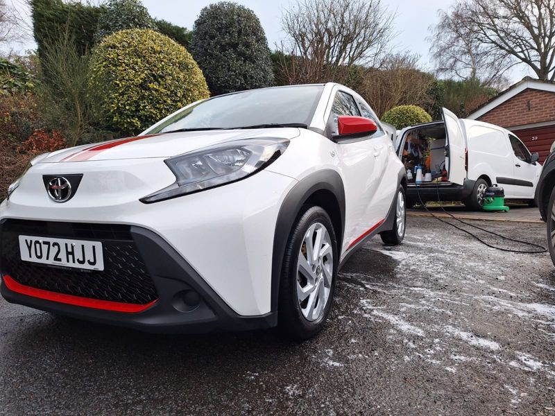 A freshly valeted white Toyota Aygo X on a client's driveway, with the valeting van behind